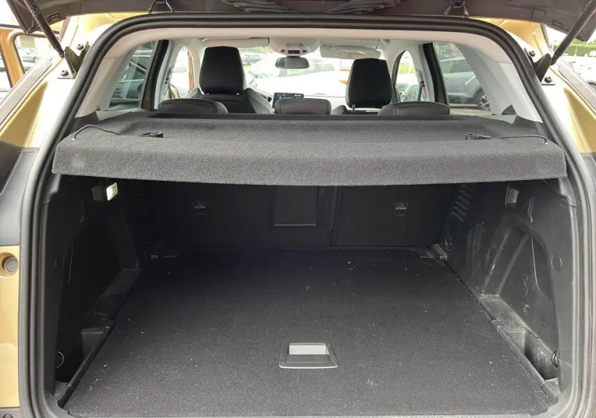 Coffre ouvert vu de l'arrière d'un Peugeot 3008 jaune clair, avec cache-bagages et sièges arrière visibles.