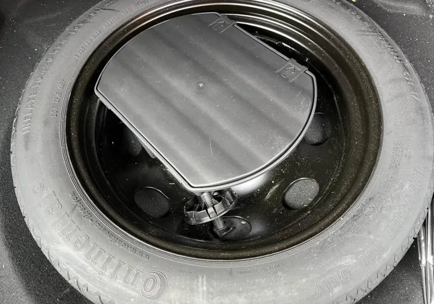 Roue de secours noire montée sur jante acier, visible dans le coffre d’un Peugeot 3008 jaune clair.