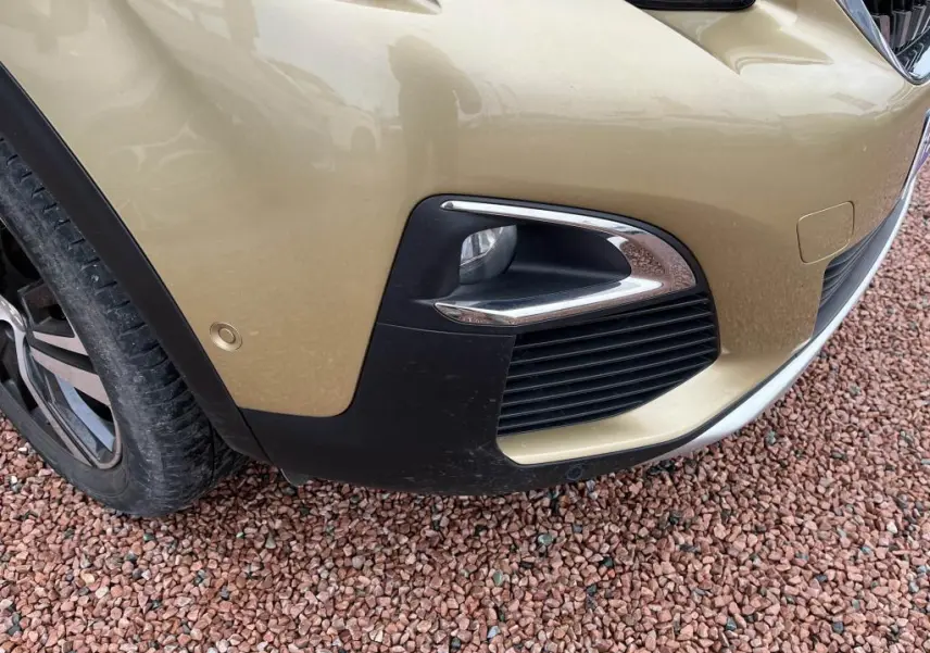 Gros plan sur le pare-chocs avant droit jaune clair du Peugeot 3008 avec antibrouillard et capteur de stationnement.