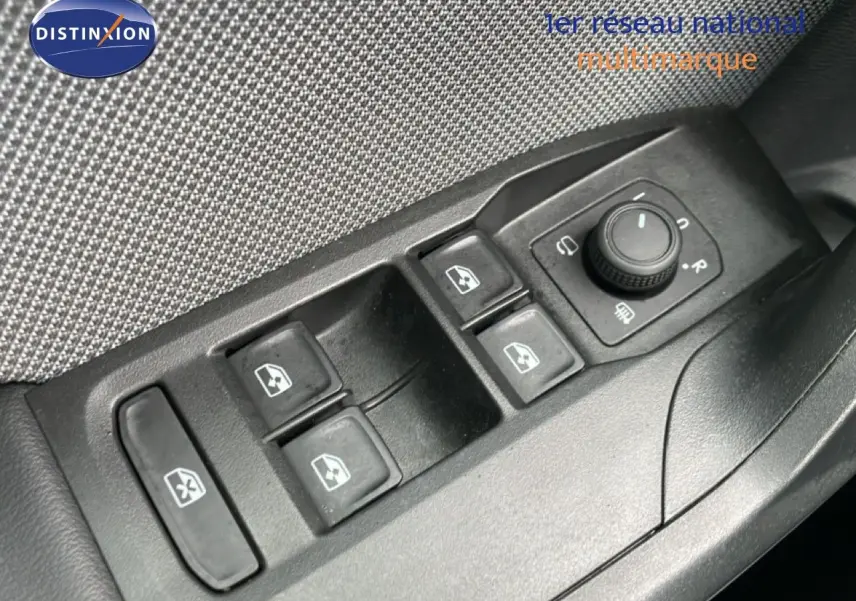 Gros plan sur les commandes des vitres électriques et rétroviseurs côté conducteur d'une SEAT Leon gris métallique.