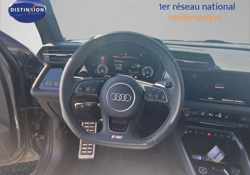 Vue intérieure centrée sur le volant sport Audi A3 Sportback gris Daytona, tableau de bord numérique et écran tactile visibles.