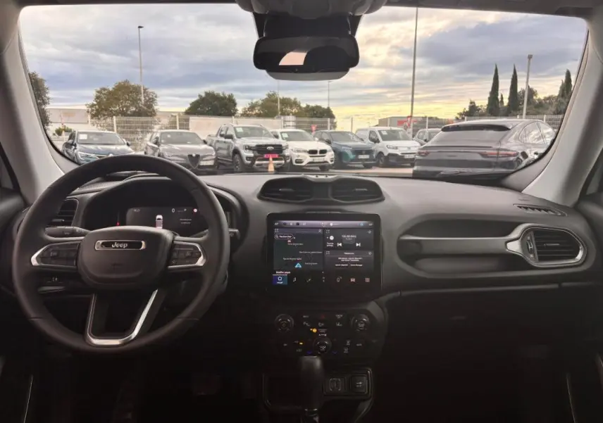 Vue intérieure frontale du tableau de bord du Jeep Renegade 2024 blanc, avec écran tactile central et volant multifonction.
