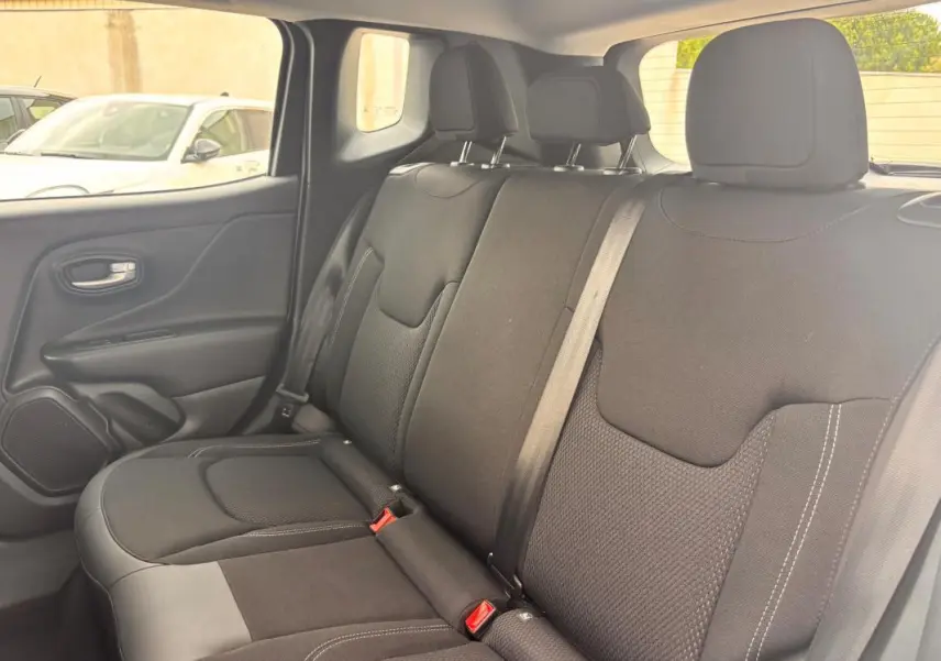 Vue intérieure arrière côté gauche du Jeep Renegade 2024 blanc, sièges tissu noir avec ceintures de sécurité visibles.