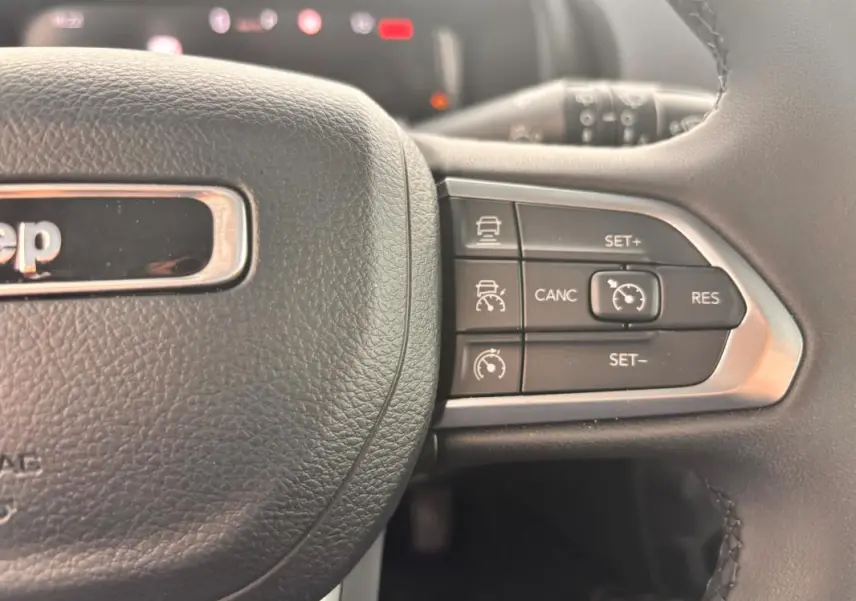 Gros plan sur les commandes de régulateur de vitesse au volant noir du Jeep Renegade 2024 blanc e-Hybrid Altitude.