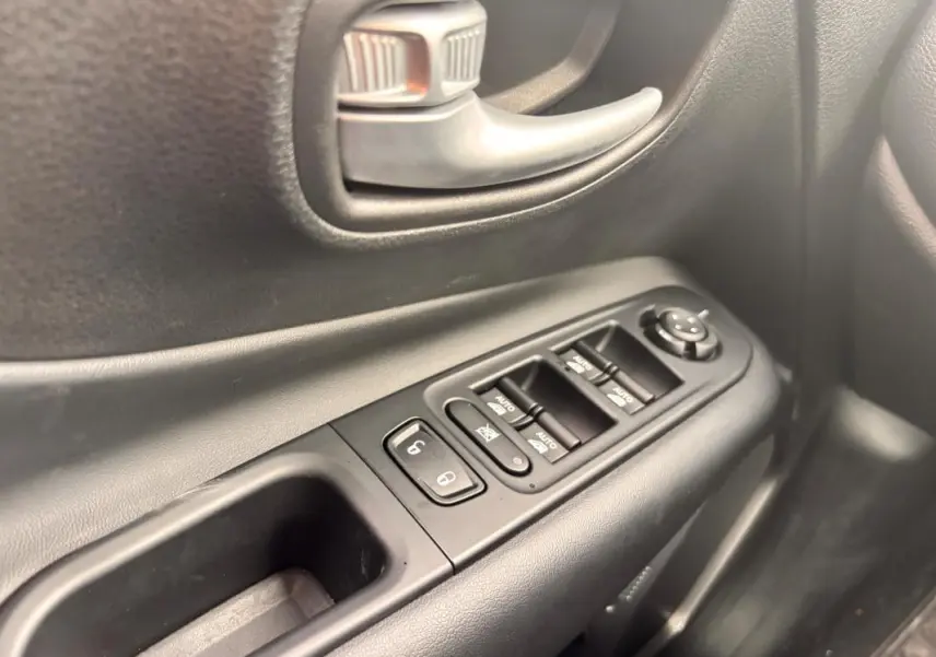 Gros plan sur la commande des vitres et la poignée intérieure côté conducteur d'une Jeep Renegade 2024 noire.