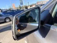 Rétroviseur extérieur côté gauche d'une Mercedes GLA 200 Fascination gris foncé métal, reflet et environnement urbain visibles.