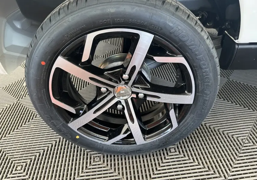 Gros plan sur la roue avant droite d’une Aixam Ambition 0.5 Crossover Premium blanche avec jante noire et argentée.