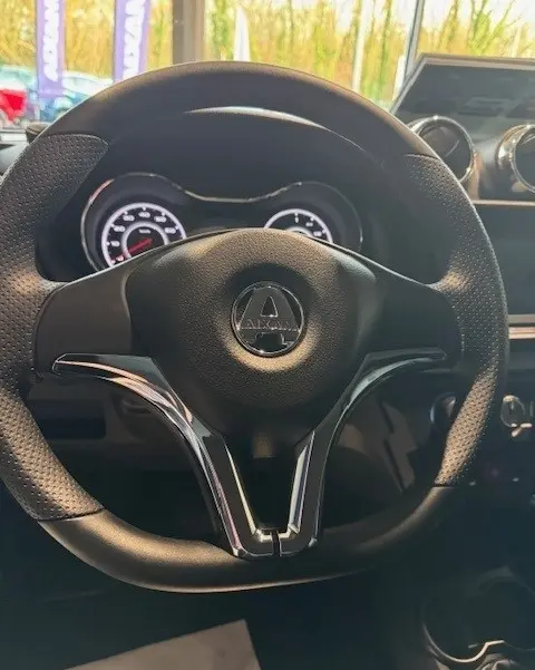 Vue rapprochée du volant noir de l'AIXAM AMBITION 0.5 CROSSOVER PREMIUM 2026 avec tableau de bord éclairé en arrière-plan.