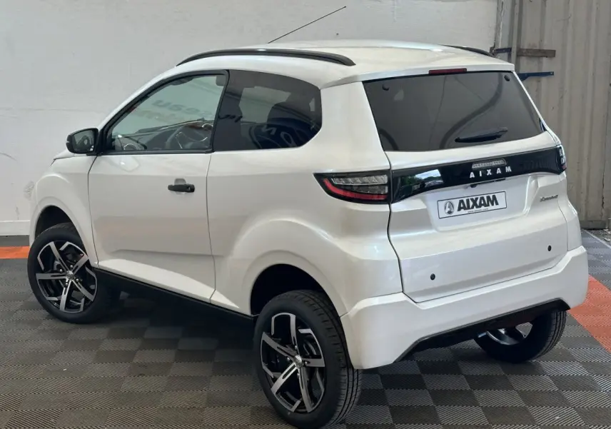 Vue 3/4 arrière droite d'une Aixam Ambition 0.5 Crossover Premium blanche avec jantes noires et rétroviseur caméra côté gauche.