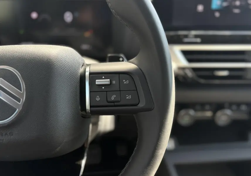 Gros plan sur les commandes gauche du volant cuir du Citroën C4 Hybrid blanc, avec tableau de bord flou en arrière-plan.