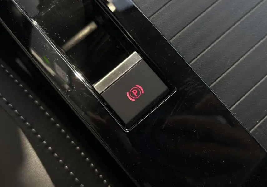 Gros plan sur le bouton de frein de stationnement électrique rouge sur console noire brillante d’une Citroën C4 Hybrid 2025.