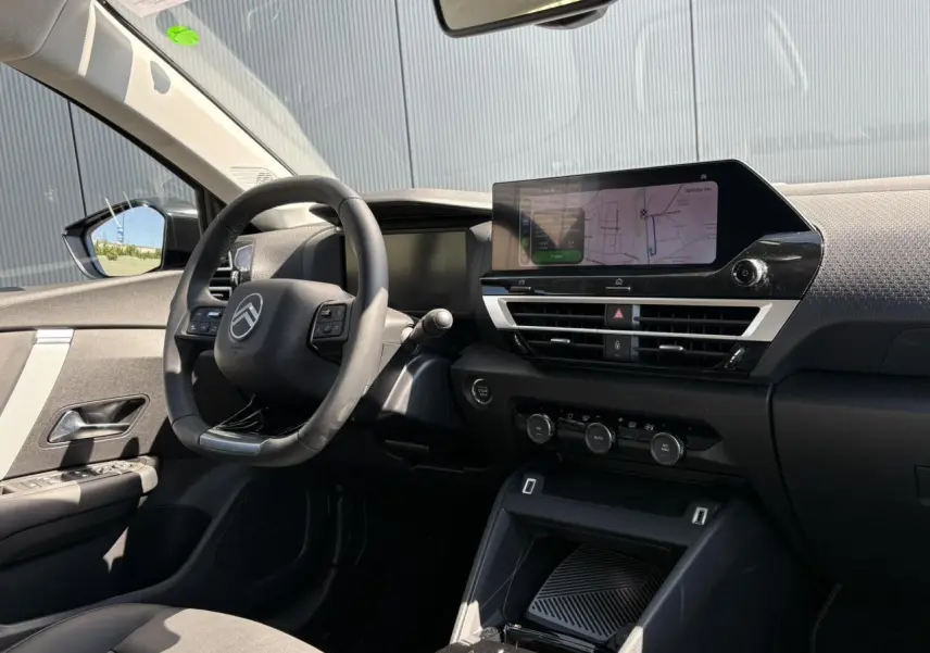 Vue intérieure côté conducteur de la Citroën C4 Hybrid 2025, avec tableau de bord noir et écran tactile GPS allumé.