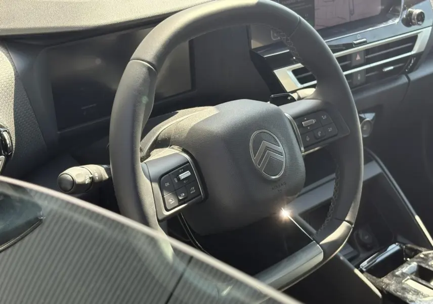 Vue rapprochée du volant cuir noir avec commandes intégrées du tableau de bord intérieur de la Citroën C4 Hybrid 2025.