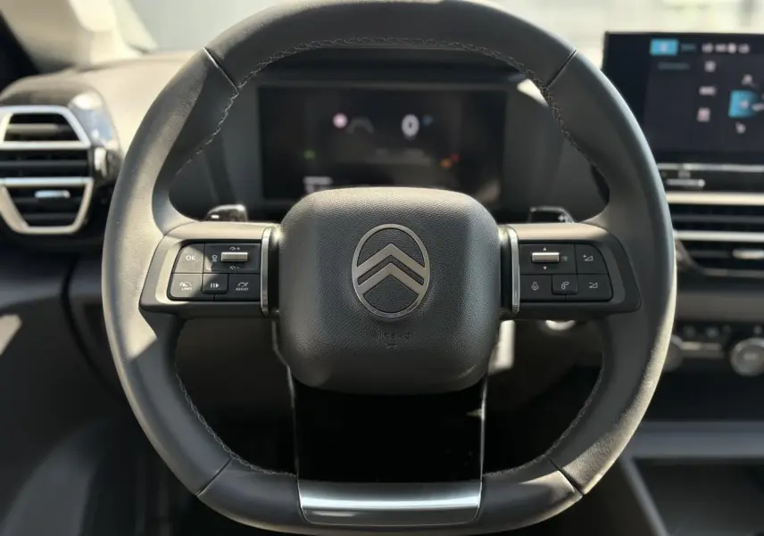 Volant cuir noir Citroën C4 Hybrid 145 vu de face avec commandes intégrées et tableau de bord numérique flou en arrière-plan.