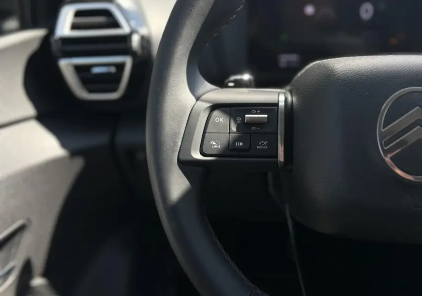 Gros plan sur le volant cuir noir côté gauche du Citroën C4 Hybrid 2025 avec commandes intégrées et logo central.