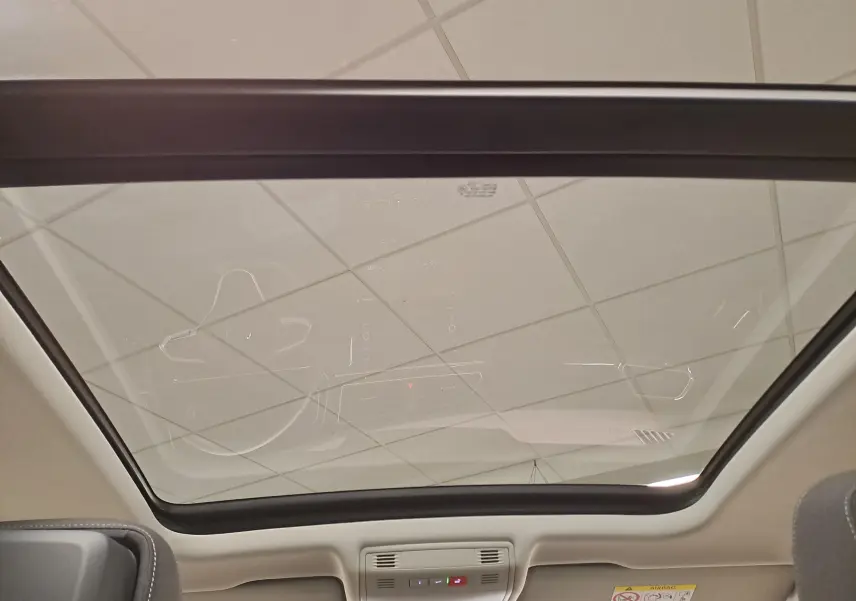 Toit panoramique vu de l'intérieur du Volkswagen Tiguan 2022 noir intense, avec ciel de toit clair et commandes intégrées.