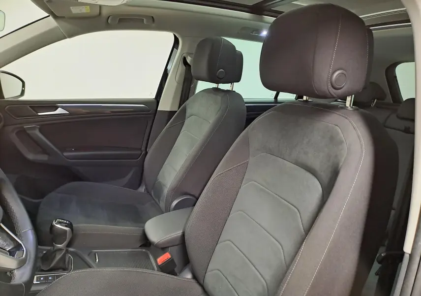 Vue intérieure côté gauche du Volkswagen Tiguan 2022, sièges tissu noir avec surpiqûres blanches et accoudoir central.
