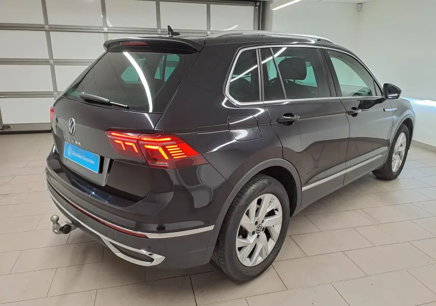 Vue 3/4 arrière droite du Volkswagen Tiguan noir intense 2022 avec feux allumés et crochet d'attelage escamotable visible.