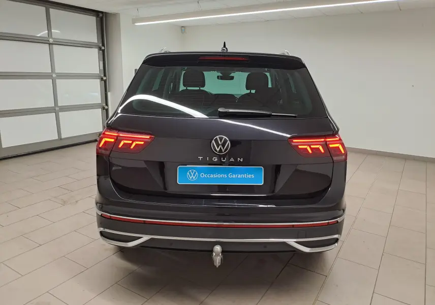 Vue arrière d'un Volkswagen Tiguan noir intense 2022 avec feux allumés et crochet d'attelage escamotable visible.