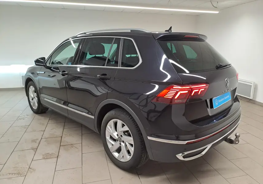 Volkswagen Tiguan noir intense vu 3/4 arrière droit, avec feux allumés et crochet d'attelage escamotable visible.