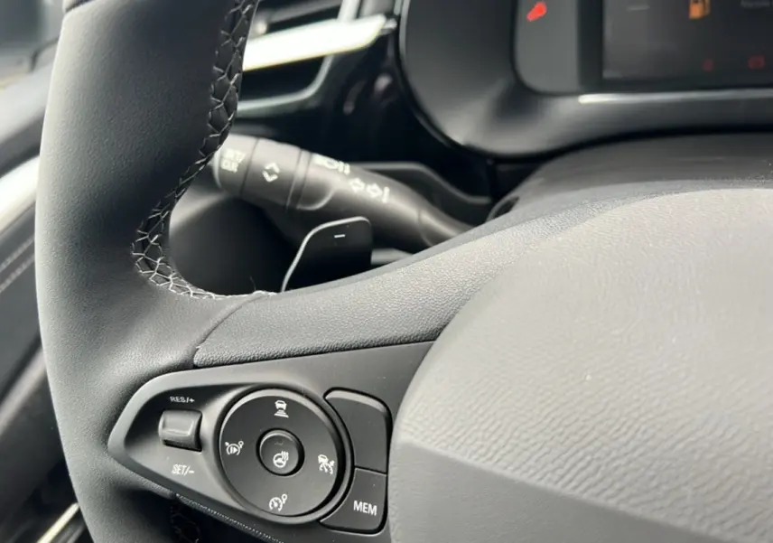 Gros plan sur le volant cuir noir de l’Opel Corsa Hybrid 110 e-DCT6, avec commandes multifonctions et bouton de chauffage.