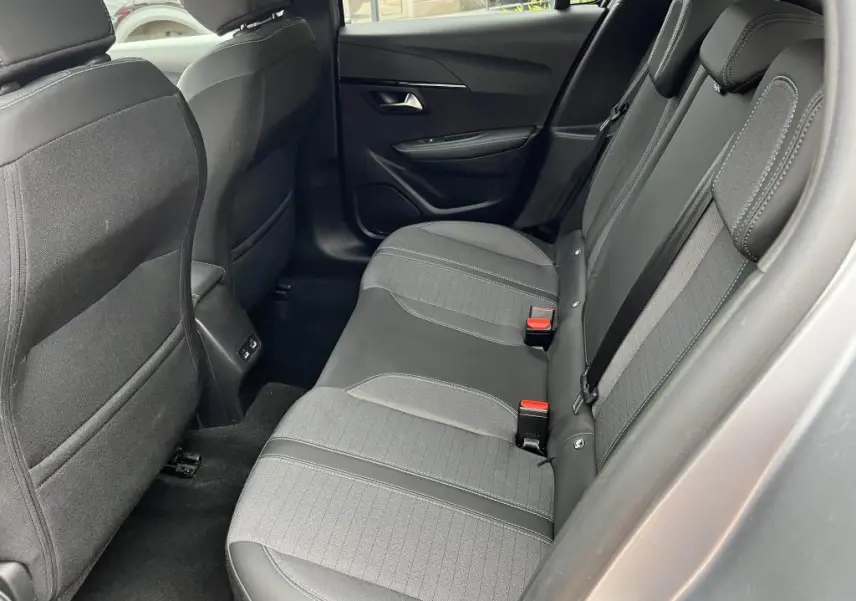 Vue intérieure arrière côté droit de la Peugeot 208 gris clair, sièges tissu noir avec surpiqûres grises et ceintures rouges.