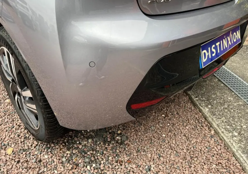 Vue rapprochée du coin arrière gauche d'une Peugeot 208 gris clair avec capteurs de stationnement et logo 208 visible.