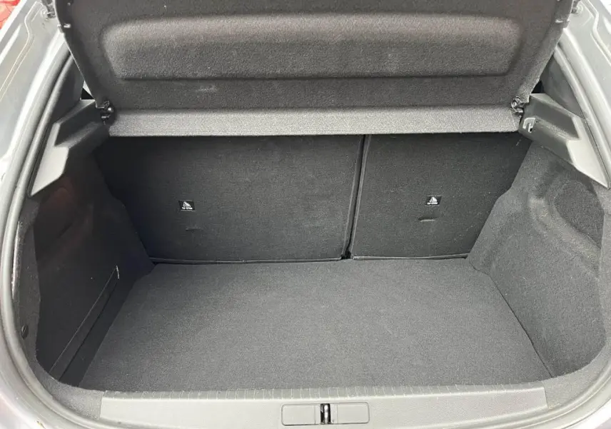 Coffre ouvert vu de l'arrière d'une Peugeot 208 gris clair, montrant un espace de chargement propre et vide.