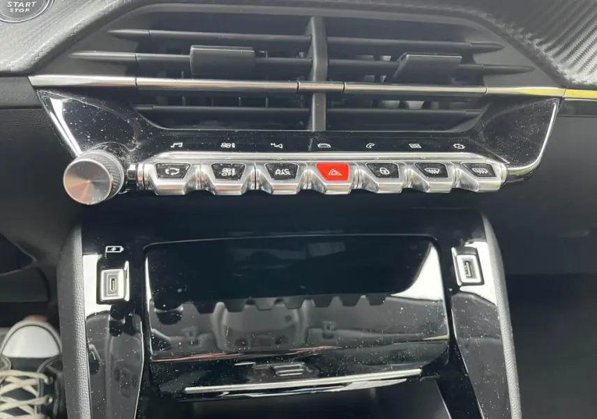 Vue rapprochée de la console centrale noire brillante de la Peugeot 208 2022 avec boutons métallisés et prise USB visible.