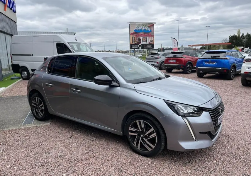 Peugeot 208 gris clair vue 3/4 avant droit, avec phares LED et jantes alliage distinctives.