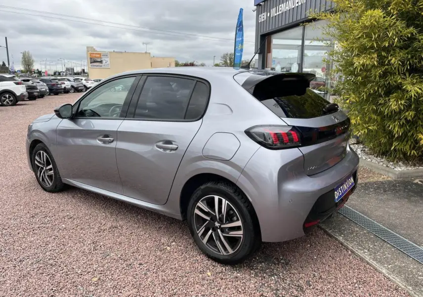 Peugeot 208 gris clair vue 3/4 arrière droit, avec vitres surteintées et jantes alliage distinctives.