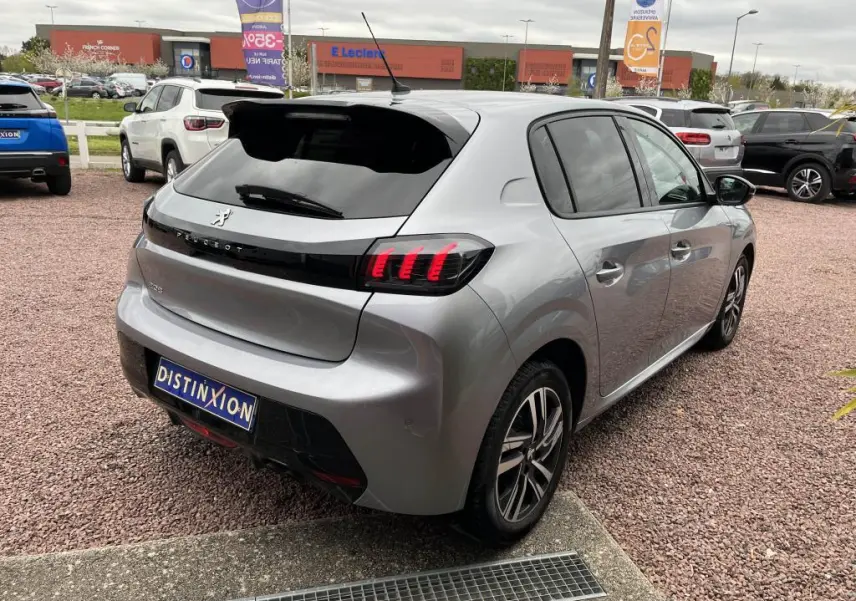 Peugeot 208 gris clair vue 3/4 arrière droit, avec feux arrière à griffes rouges et jantes alliage bicolores.