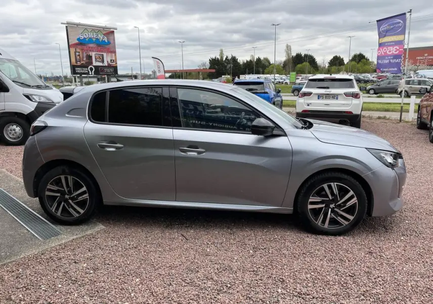 Peugeot 208 gris clair vue de profil côté gauche, avec vitres arrière surteintées et jantes alliage.