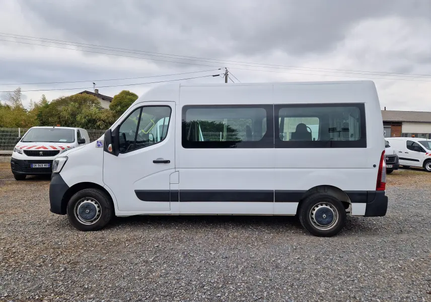 Vue de profil côté gauche d’un Renault Master blanc TPMR avec rampe arrière et marchepied porte latérale sur un terrain gravillonné.