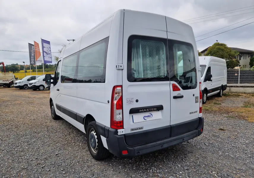 Vue 3/4 arrière droite d’un Renault Master blanc avec vitres latérales teintées et porte arrière double, stationné sur un sol gravillonné.