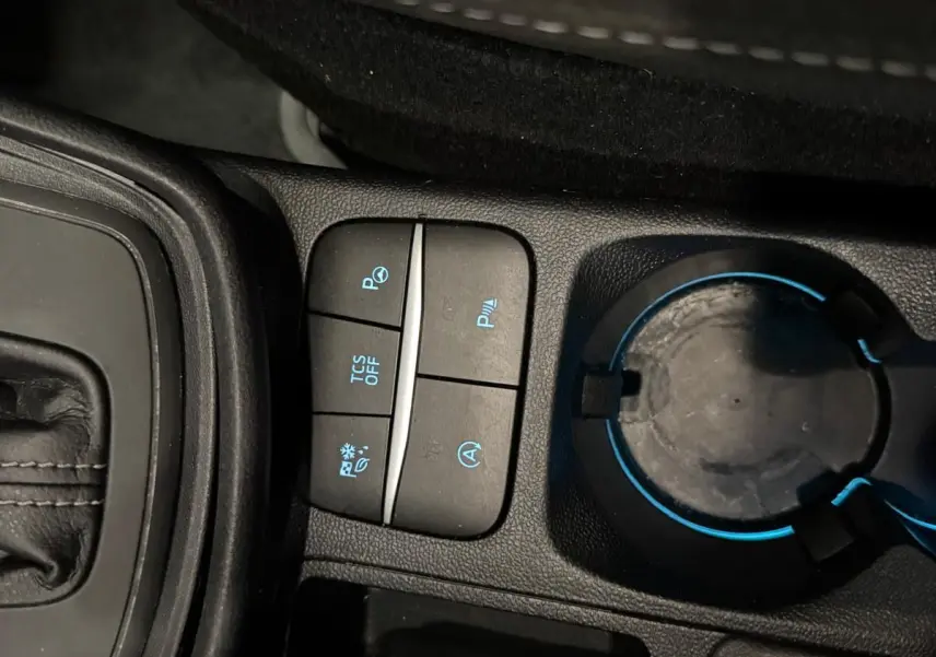 Gros plan sur la console centrale du Ford Puma gris Solar 2023, avec boutons de contrôle et porte-gobelet éclairé.