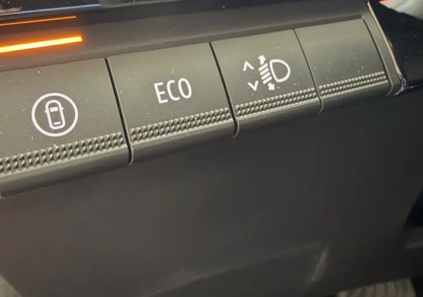 Gros plan sur les boutons de commande intérieurs de la Renault Clio 2025 rouge, avec mode ECO et réglage des phares.