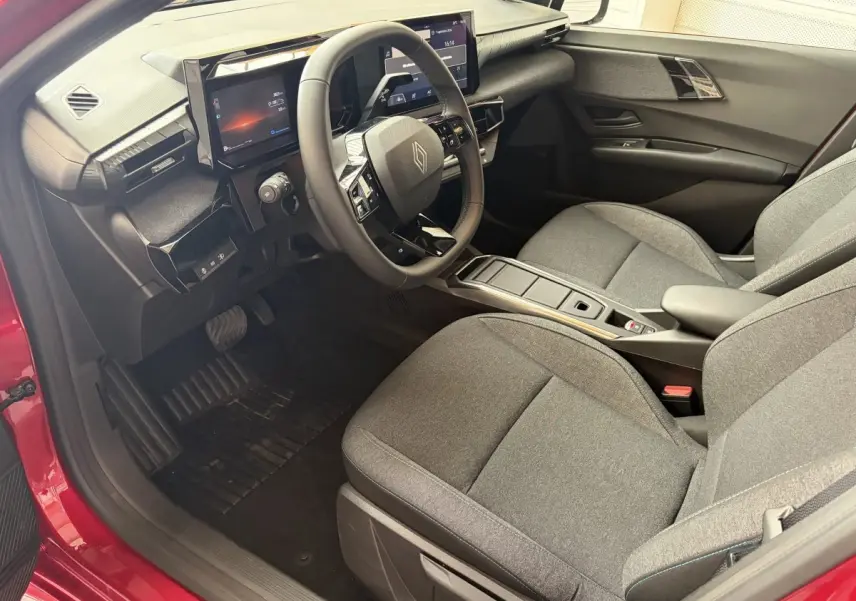 Intérieur avant droit de la Renault Clio Evolution rouge 2025, avec tableau de bord numérique et sièges tissu gris.