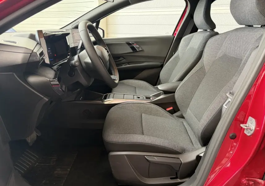 Intérieur côté conducteur de la Renault Clio rouge 2025, montrant sièges gris et tableau de bord moderne avec écran tactile.