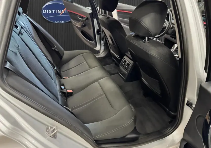 Vue intérieure côté arrière gauche de la BMW Série 3 Touring gris aluminium, montrant les sièges noirs et la porte ouverte.