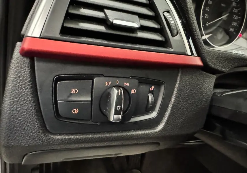 Gros plan sur le bouton de commande des phares avec bande décorative rouge dans l’habitacle noir d’une BMW Série 3 Touring F31.