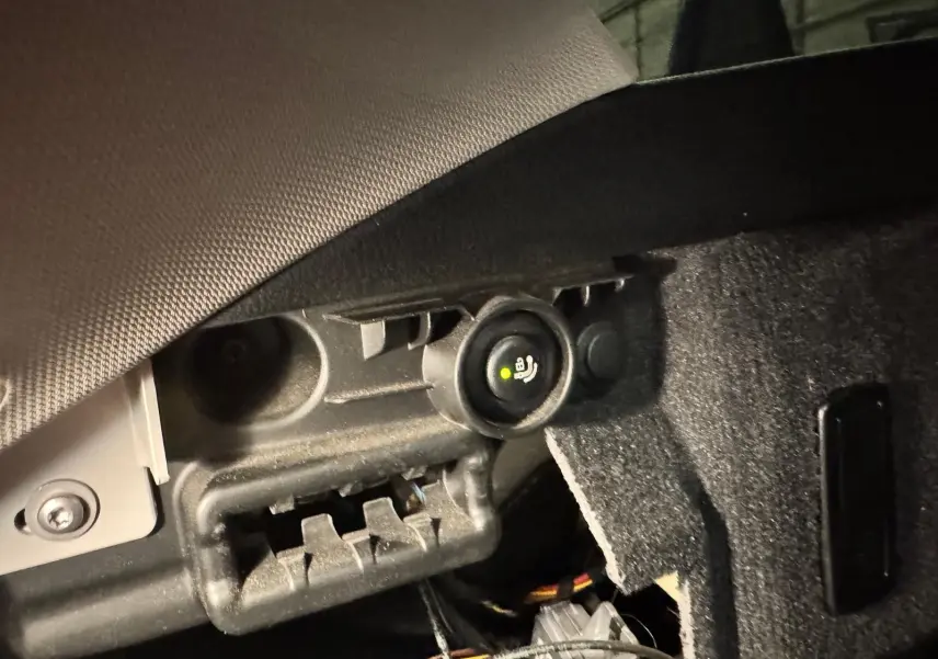 Détail de l'attelage électrique sous le coffre d'une BMW Série 3 Touring F31 gris aluminium, avec prise et bouton de commande.