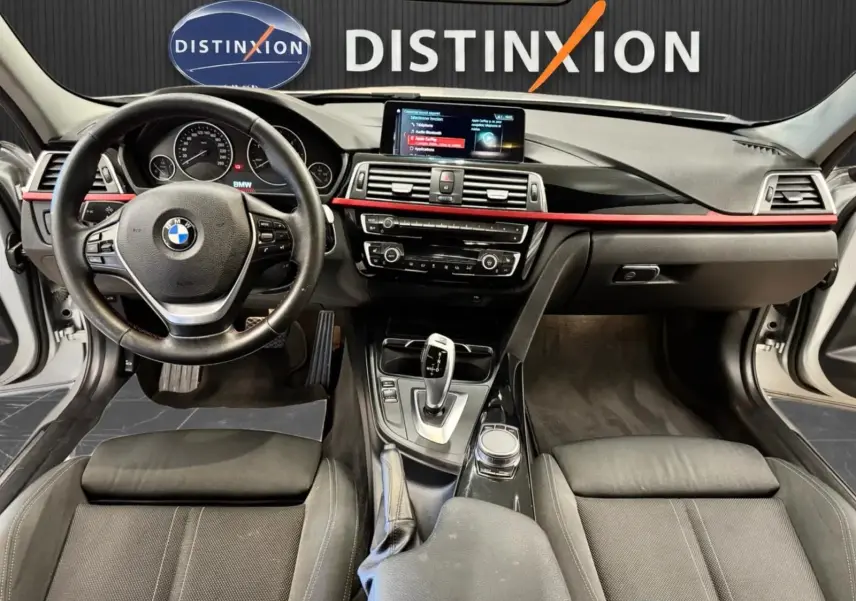 Vue intérieure avant de la BMW Série 3 Touring F31 320d XDrive 2018, tableau de bord noir avec bande rouge et écran central.