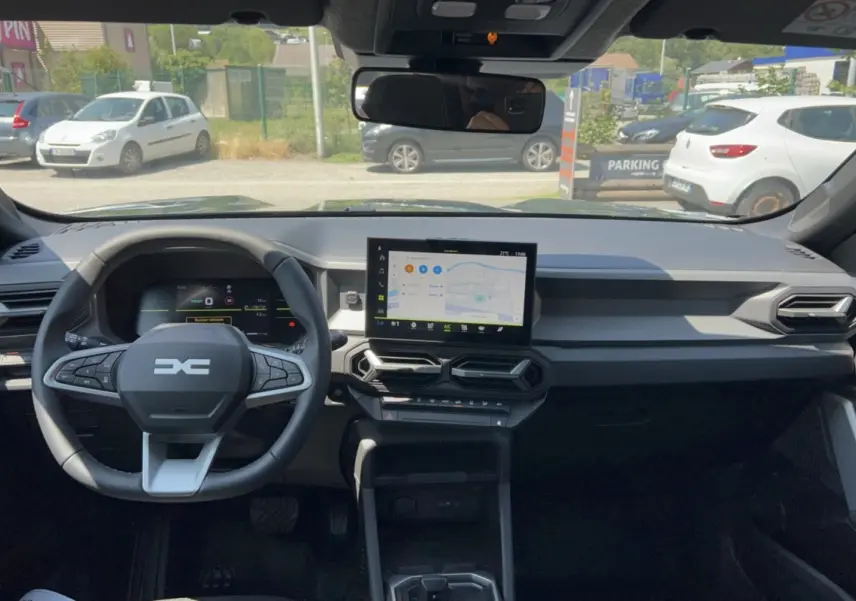Vue intérieure frontale du tableau de bord du Dacia Duster Hybrid-G 150 avec écran central tactile et volant multifonction.