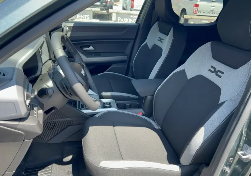 Vue intérieure côté conducteur du Dacia Duster Hybrid-G 150 4x4 en vert cèdre, sièges bi-ton avec logo distinctif sur appuie-tête.