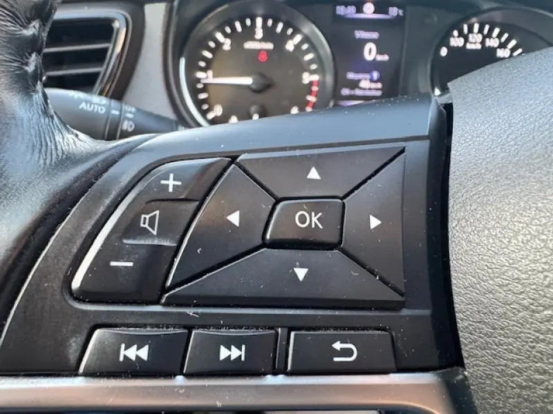 Gros plan sur les commandes au volant noir du Nissan X-TRAIL 2018 avec tableau de bord en arrière-plan flou.