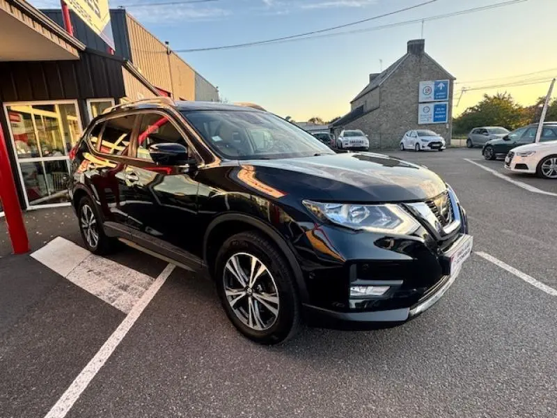Nissan X-Trail noir intense vu en 3/4 avant droit, avec jantes alliage et barres de toit visibles.