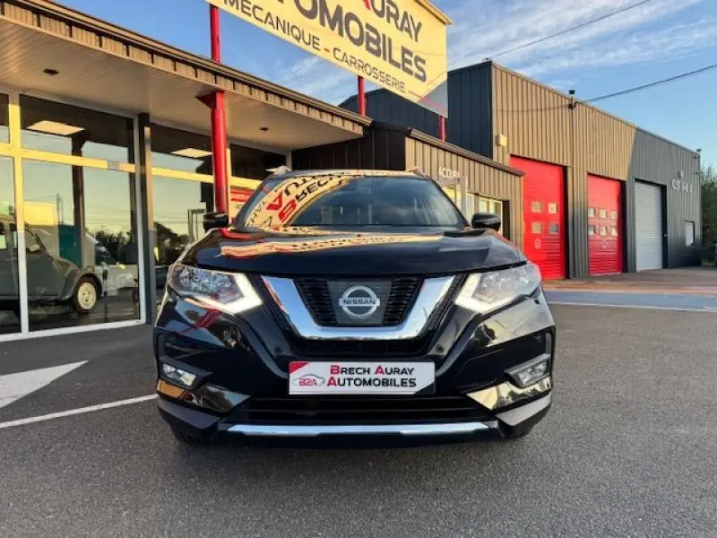 Vue avant d'un Nissan X-Trail noir intense avec calandre chromée et feux LED allumés devant un garage.
