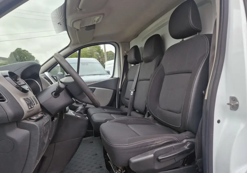Vue intérieure côté conducteur du Renault Trafic Fourgon blanc 2019, montrant les sièges noirs et le tableau de bord.