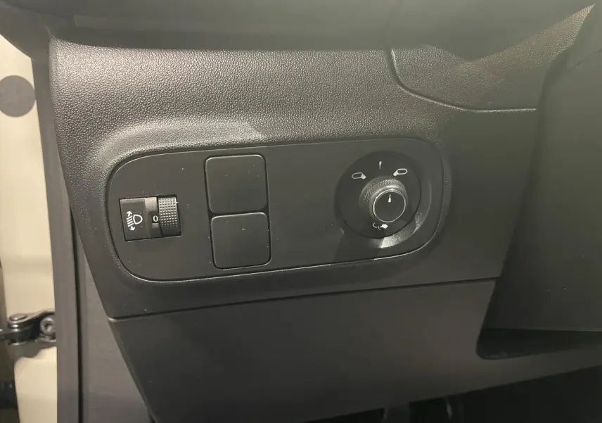 Vue intérieure côté gauche de la porte beige clair d'une Citroën C3 2024 avec commandes de réglage des rétroviseurs et phares.